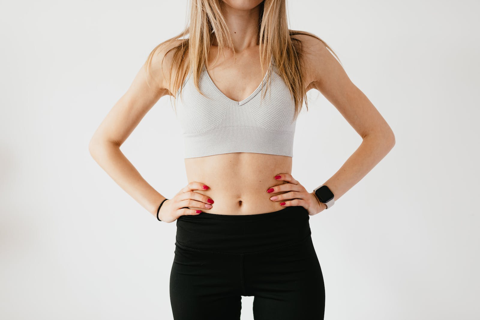 Faceless slim anonymous blond female in sports bra and black leggings in wearable bracelet showing perfect belly