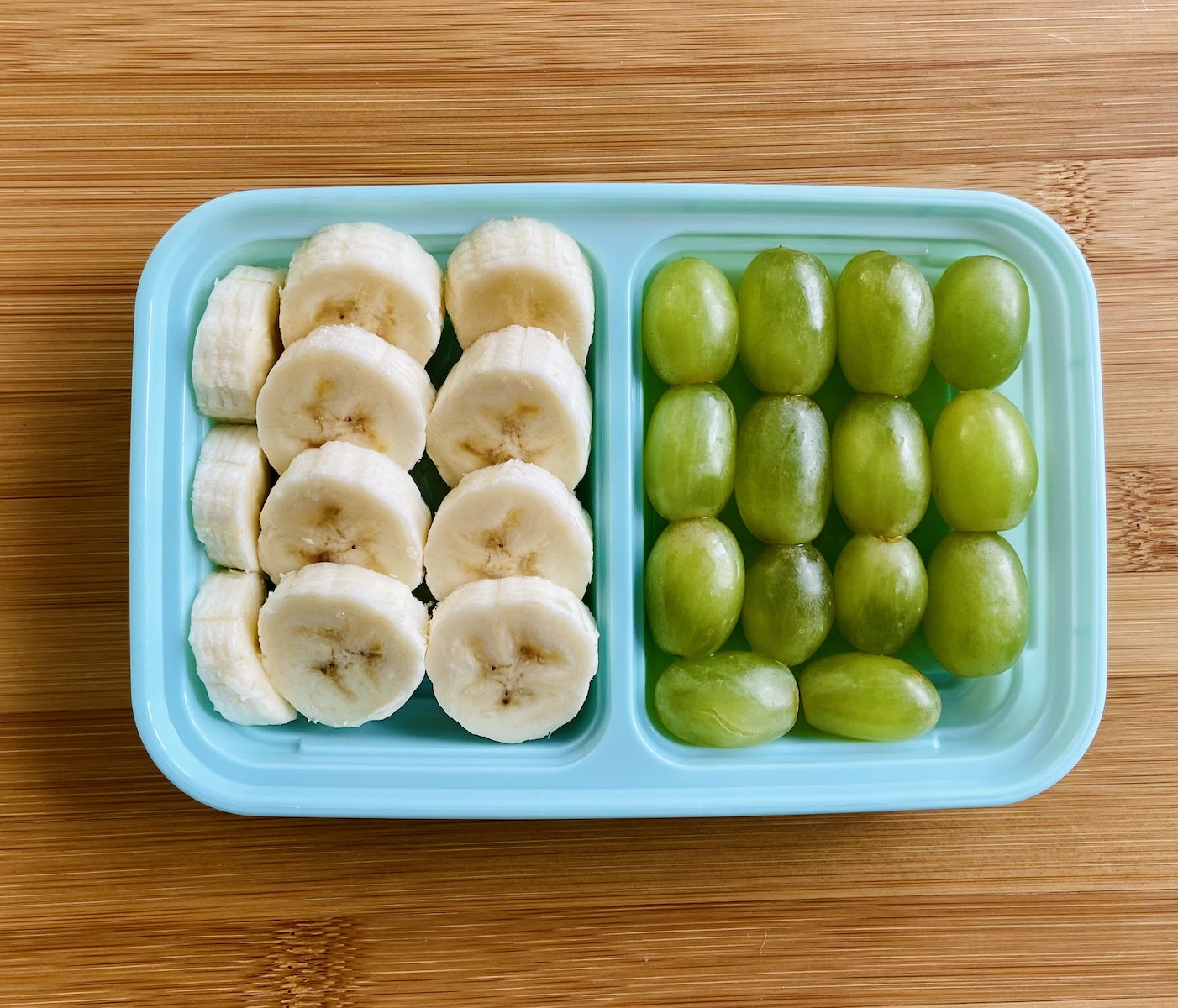 A Sliced Banana and Green Grapes on a Plastic Container
